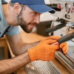 Smiling young man repairing coffee machine in cafe